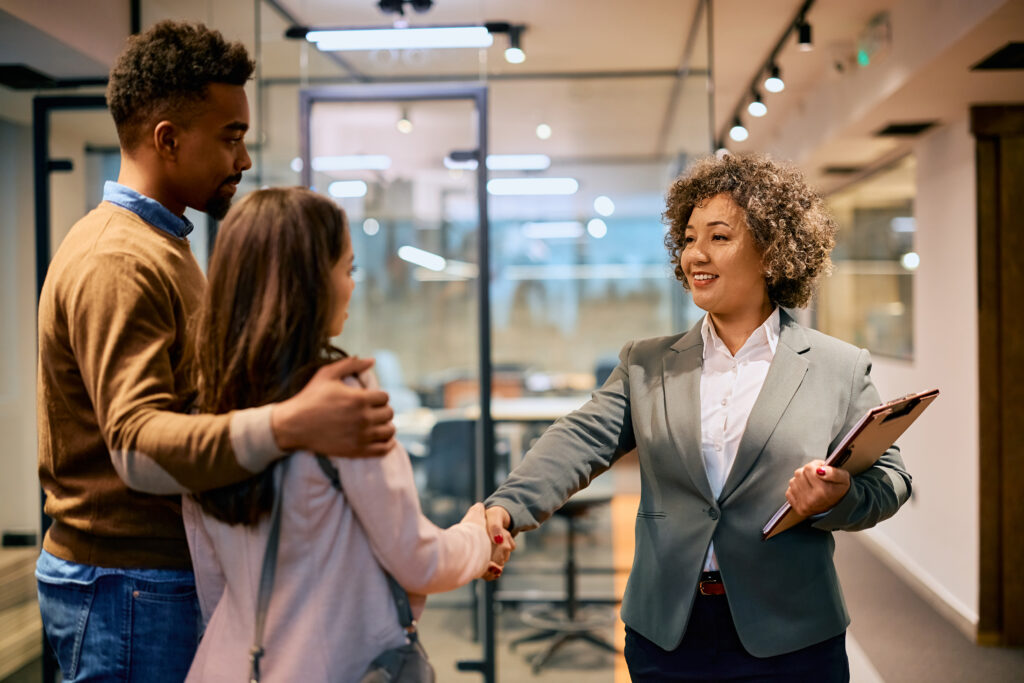 Happy financial consultant and African American couple handshaking in the office.